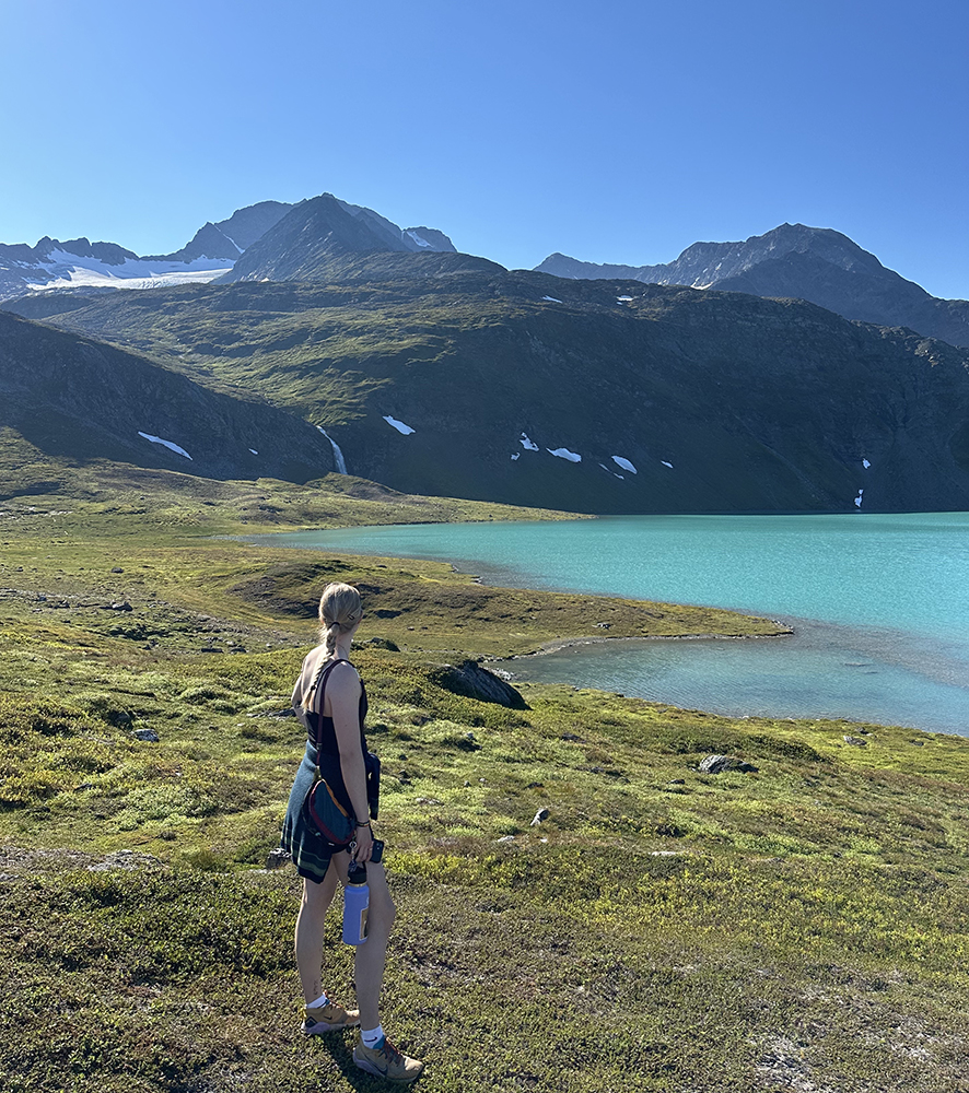 Amalie standing at a teal blue lake surrounded by mountains.