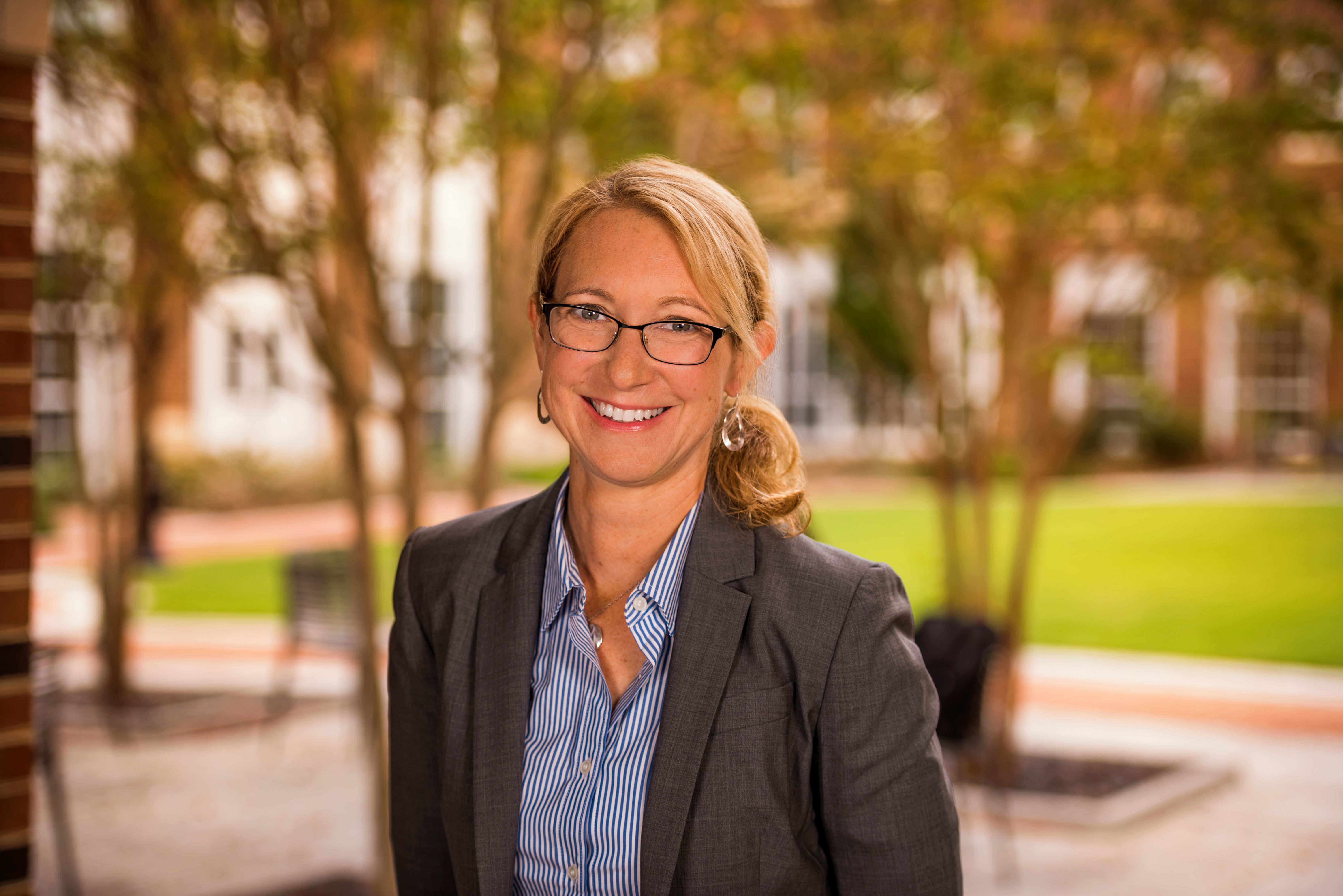 Smiling woman in glasses and gray blazer, outdoor campus portrait
