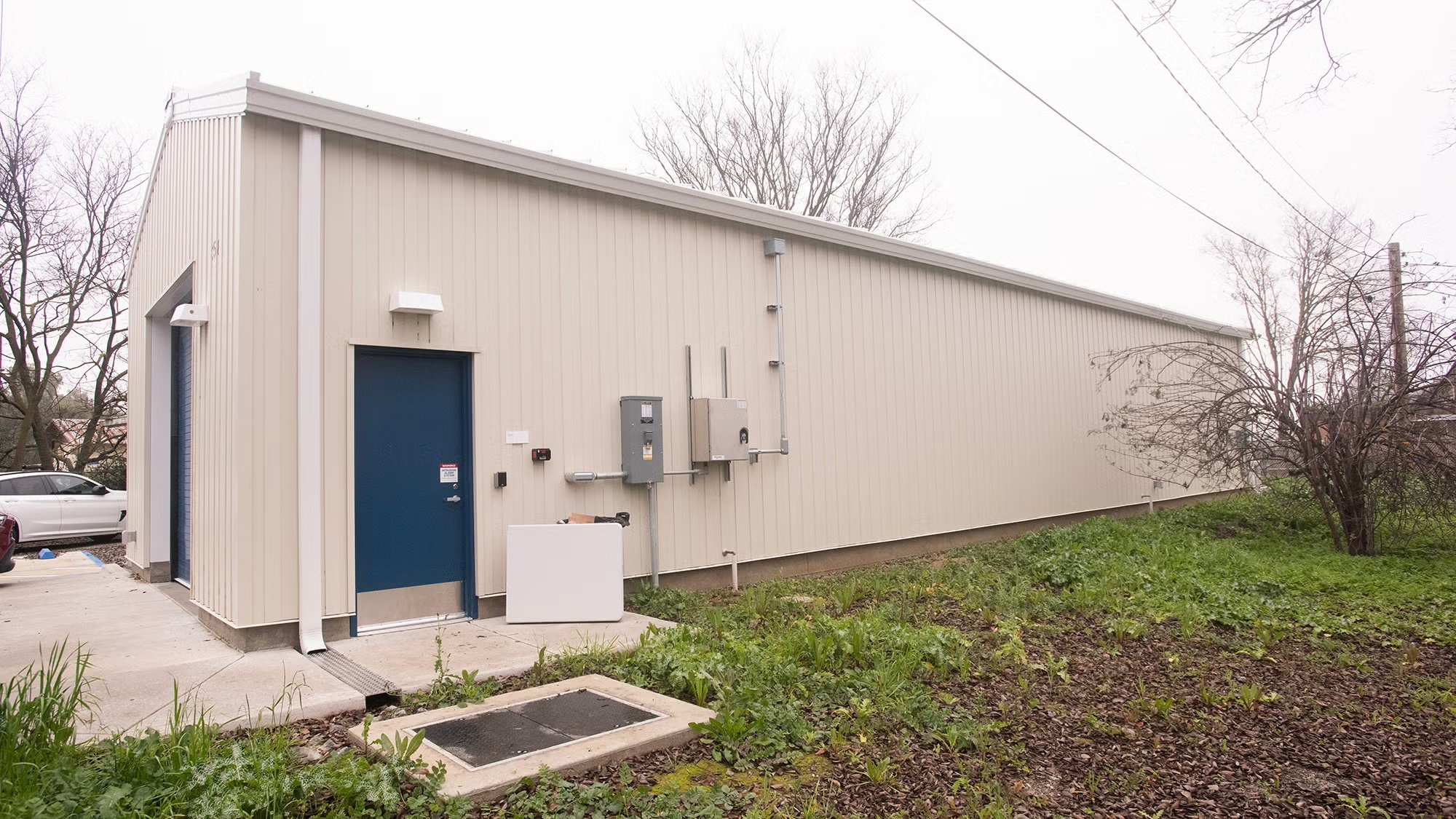 A small, light-colored industrial building with blue doors, surrounded by grass.