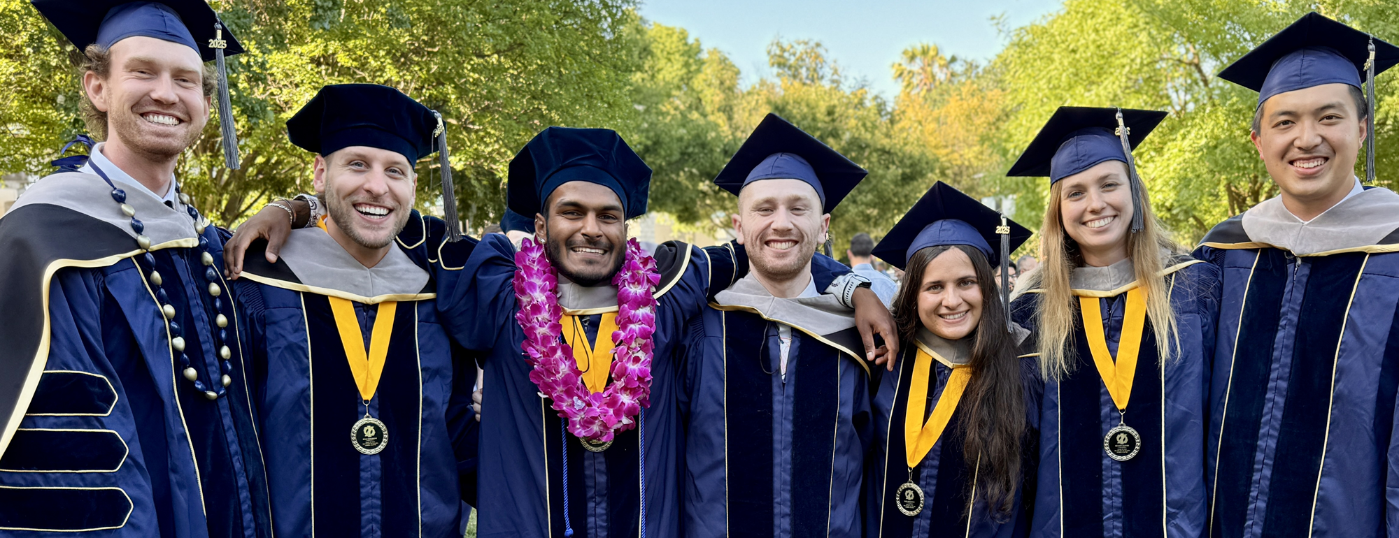 A group of graduates wearing caps and gowns posing outside.
