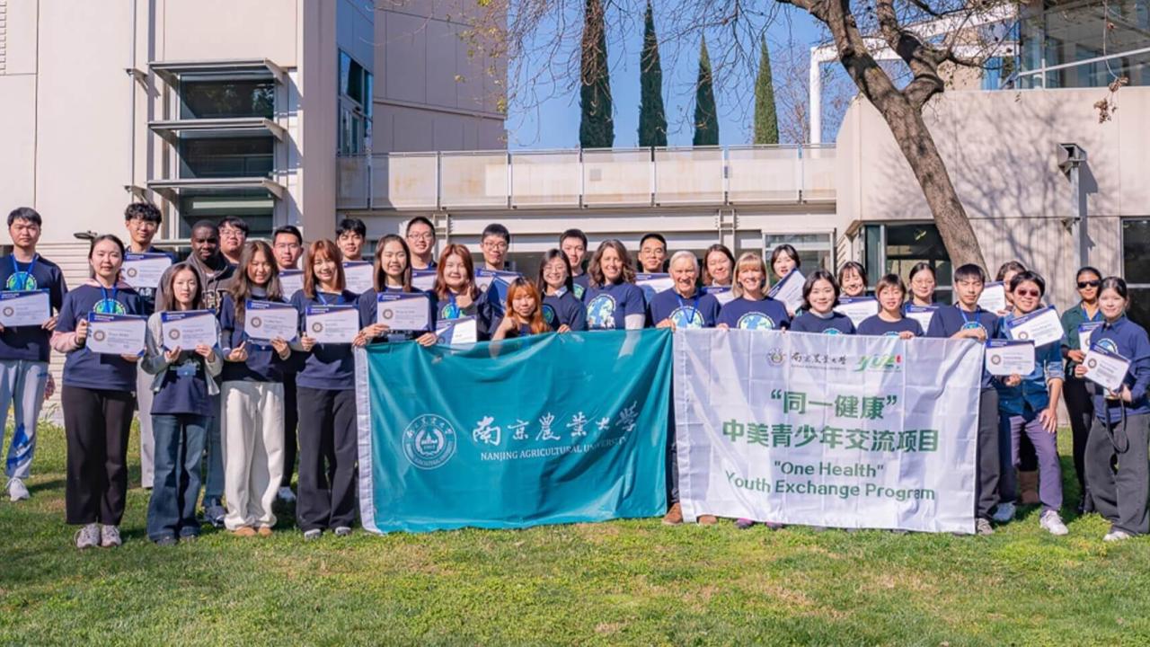 Group photo of students on grass holding two banners in front of a campus building