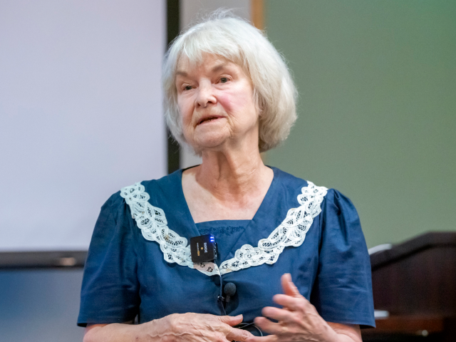 Dr. Lynette Hart standing in front of a screen and podium in a lecture hall.