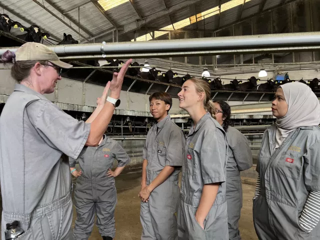 Instructor gesturing to trainees in gray coveralls inside a large aircraft hangar