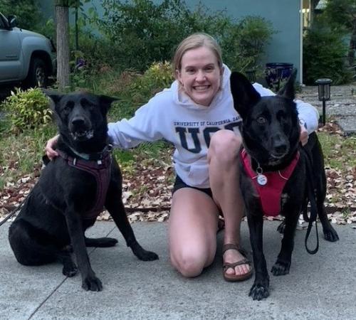 two black German shepherds sitting on each side of a woman