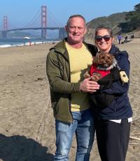 man and woman holding small dog on beach in San Francisco with the Golden Gate Bridge in the background