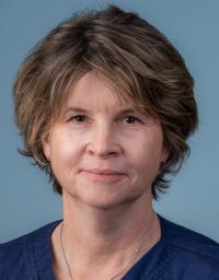 Middle-aged woman, short brown hair, blue top, neutral expression — portrait photograph