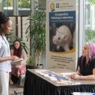 young woman standing speaking to woman sitting at a table during a conference