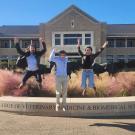 three students jumping for joy in front of a college building